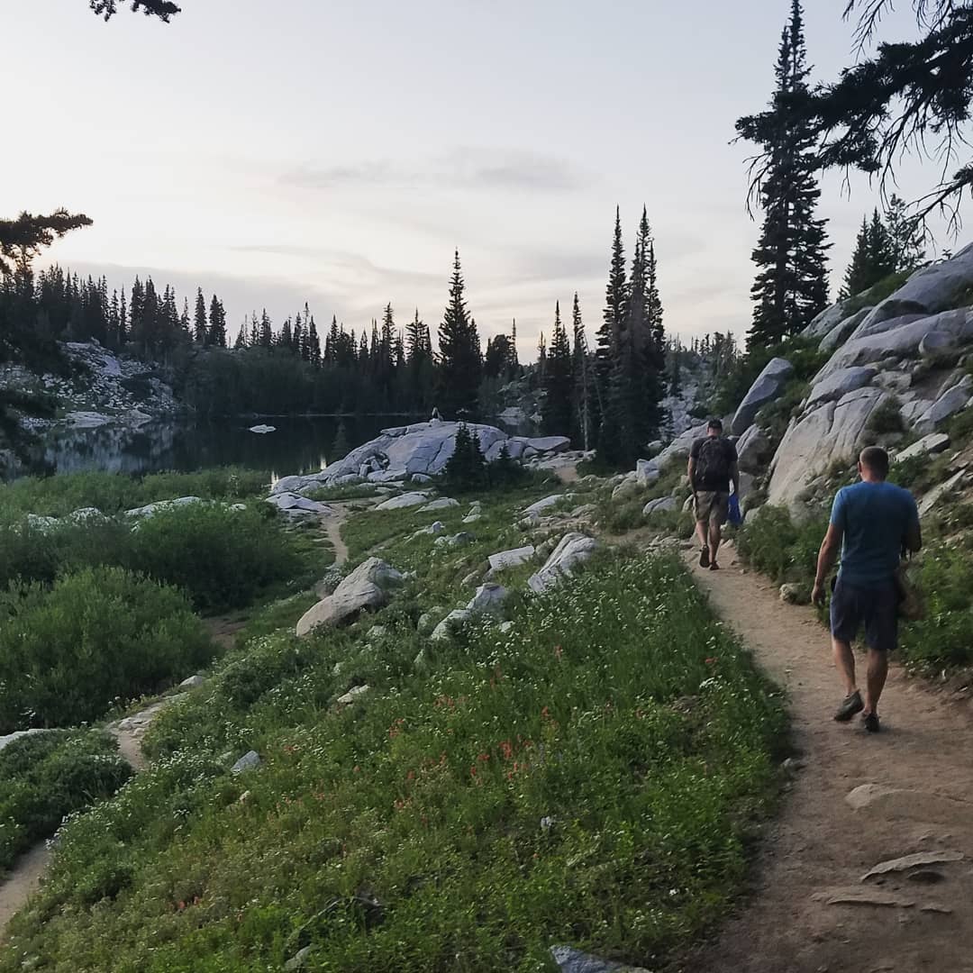 Two hikers on a granite alpine trail beside a mountain lake at dusk